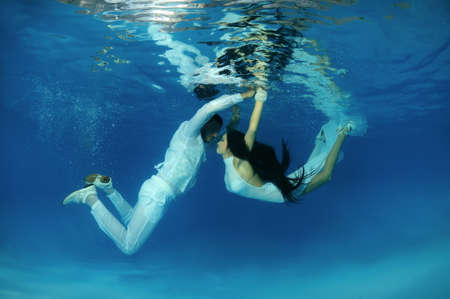 Bride and groom in a white wedding dress swim to each other underwater in the pool. Underwater weddingの写真素材