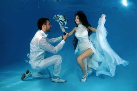 Groom kneeling offers the bride an engagement ring underwater in the pool. Underwater wedding の写真素材