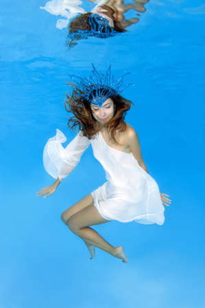 The Snow Queen - The young beautiful woman in a crown and white dress posing under water (for...