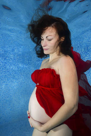Pregnant woman in a red dress posing underwater in the poolの写真素材