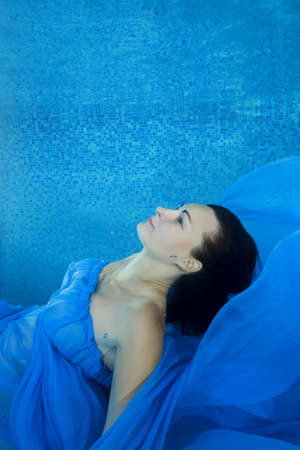 Pregnant woman in a blue dress posing underwater in the poolの写真素材