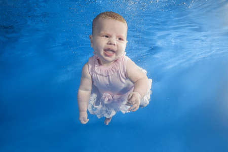 Little girl in a pink dress swims underwater in the poolの写真素材