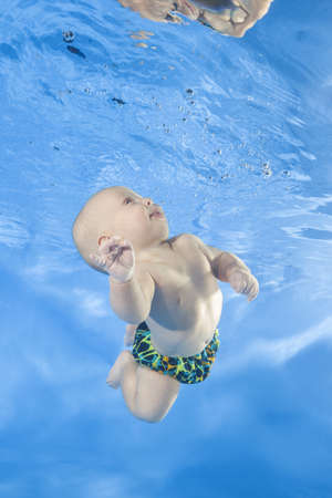 4 months boy dives underwater and looks at his reflection on the surface of the water in the poolの写真素材