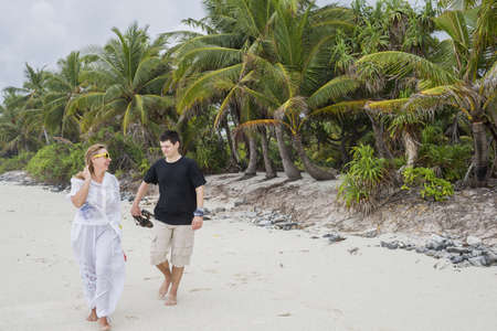 Happy young couple walking along a beautiful tropical sandy beach. Honeymoon on an exotic island. Honeymoon beautiful couple on an exotic beach. Couple in love travel on honeymoon on exotic island. Honeymoon beautiful couple on exotic beachの写真素材