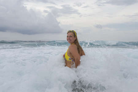 Young woman in a yellow bikkini bathes in the waves in the sea foam on an exotic tropical islandの写真素材