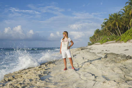 Young woman in summer dress standing on a beach and looking to the horizon on an exotic tropical islandの写真素材