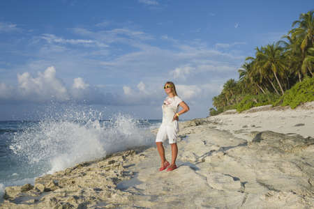 Young woman in summer dress standing on a beach and looking to the horizon on an exotic tropical islandの写真素材