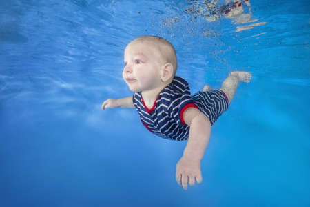 Little boy in a striped suit swim underwater on a blue water background.  Healthy family lifestyle and children water sports activity. Child development, disease preventionの写真素材