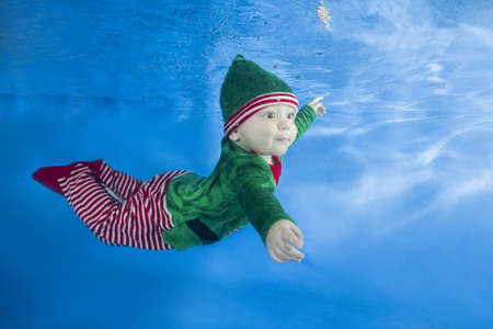 Little boy dressed as a gnome underwater on a blue water background.  Healthy family lifestyle and children water sports activity. Child development, disease preventionの写真素材