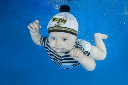 Little boy in a sailor suit swims underwater on a blue water background. Healthy family lifestyle...