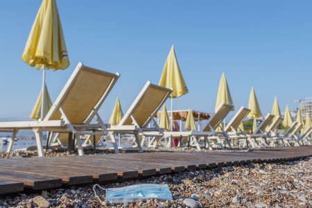 BECICI AND BUDVA, BUDVA MUNICIPALITY, MONTENEGRO - JULY 31, 2020:  Discarded used face mask lies on a beautiful pebble beach, sun loungers and beach parasols in the background.の写真素材
