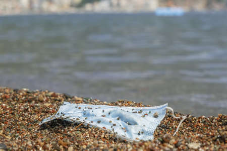 BECICI ANDi BUDVA, BUDVA MUNICIPALITY, MONTENEGRO - JULY 31, 2020: Close-up of a discarded used face mask lies in the surf zone on a sandy pebble beach.の写真素材