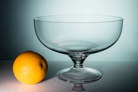 Empty transparent glass vase with an orange on a gradient backgroundの写真素材