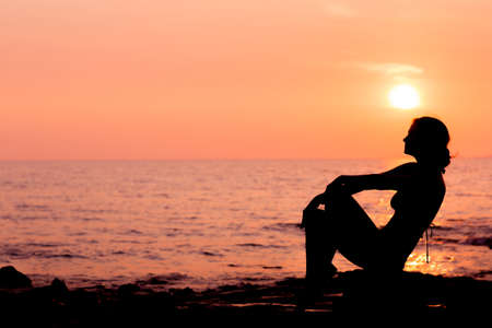 Woman silhouette sitting on sunset sea background back litの写真素材