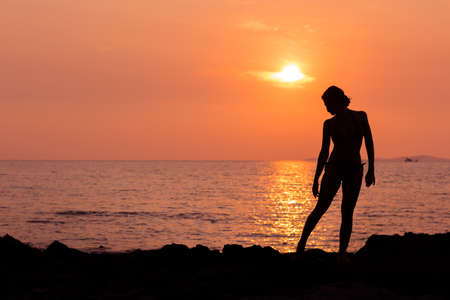 Standing woman silhouette on sunset sea background back litの写真素材