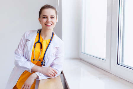 Doctor beautiful girl smiling. portrait in yellow uniform with a stethoscope near the window. Health care. background.の写真素材