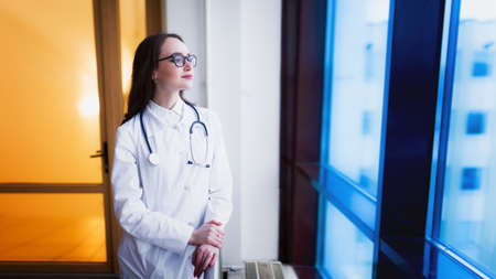 Medical student beautiful young girl with glasses, in the university near the window. The doctor smiles after the end of the working day.の写真素材