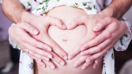 pregnancy concept - couple making a heart shape with their hands on the pregnant bellyの写真素材