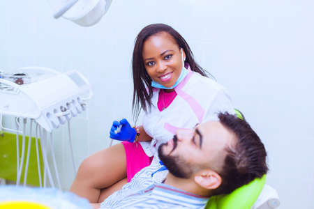Happy female black dentist talking to patient at desk in clinicの写真素材