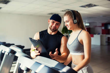 Young fitness woman exercising on a stepper with personal trainer at the gym, evaluation of the...