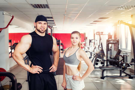 two professional personal trainers: muscular man and girl fitness instructor - with a smile watching the camera, in the gym. The concept of sport and healthy lifestyle.の写真素材