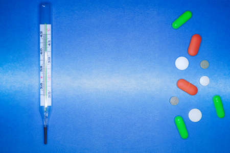 Medical thermometer and color pills on a blue background. healthcare and first aid concept.の写真素材