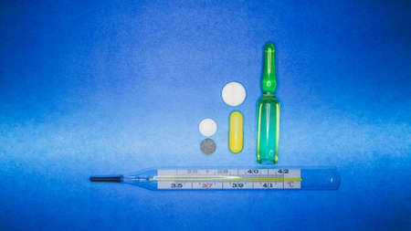Medical thermometer and color pills on a blue background.