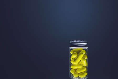 Yellow capsules in a transparent glass bottle of medium size, isolated on a dark background. Natural supplements for health. Studio lighting.の写真素材