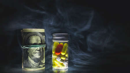 Medicine red, white and yellow pills or capsules, and bunch of money on black background shrouded in smoke with copy space. Drug prescription for treatment medication. Pharmaceutical drugs banner. Antibioticの写真素材