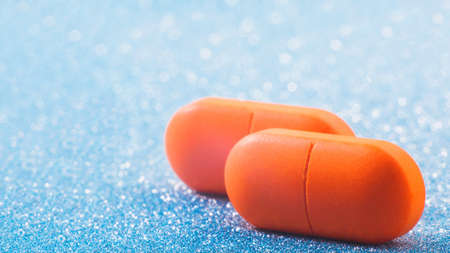 two red pills close up on blue glitter, sparkles, sparkling background copy space. Global healthcare concept. Antibiotics drug resistance. Glimmer, sequins, bokeh effect.の写真素材