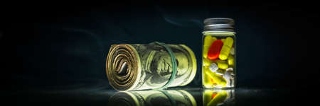 Medicine pills or capsules red, white and yellow, and bunch of money on black background shrouded in smoke with copy space. Drug prescription for treatment medication. Pharmaceutical drugs banner concept. Antibiotic.の写真素材