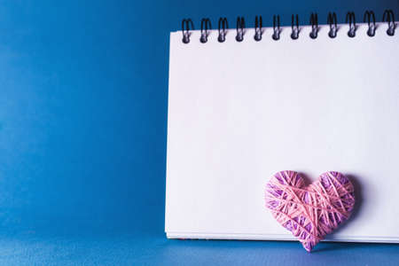 Simple blue background with a small purple red heart yn notebook. Place for text