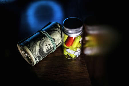 Rolls of money, Us dollars and prescription drugs on dark surface.の写真素材