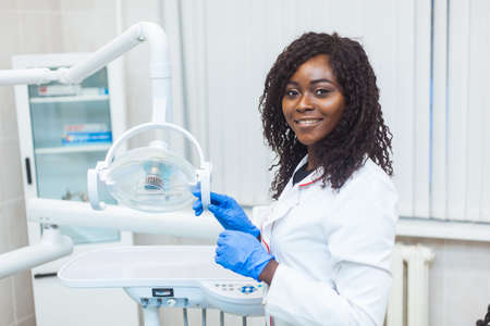 Portrait of Female black dentist in dental office. She standing at her office and she has beautiful smile. Modern medical equipmentの写真素材