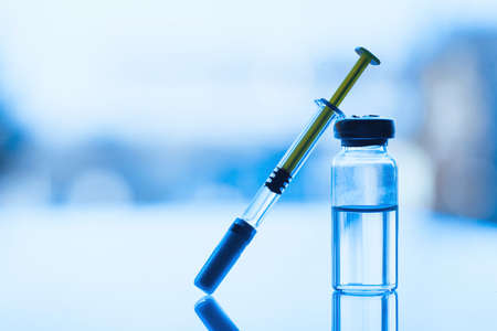 Vials of medication and syringe on a blue glass table with window background. Horizontal composition. Foreground. Vaccination conceptの写真素材