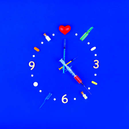 Medical pharmaceutical concept. Watch from tablets, ampoules and syringes. Medication time on a blue background. The idea of helping patients with heart disease. Heart Clockの写真素材