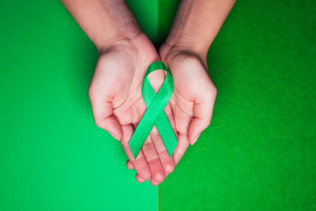 Jade tape in support of patients with hepatitis B and hepatocellular carcinoma. Green ribbon on female hands on grass backgroundの写真素材