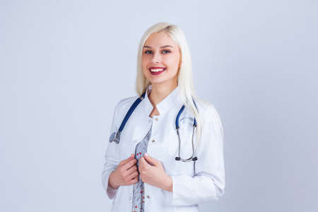 Medical concept of beautiful female doctor in white coat with phonendoscope. Medical student general practitioner. Woman hospital worker looking at camera and smiling, studio, gray background.の写真素材