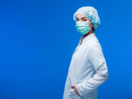 Young female nurse at camera wearing surgical mask and suit. Covid-19 pandemic.