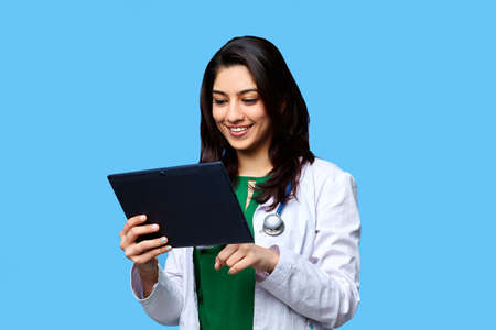 Beautiful young Asian girl doctor, with a laptop for records isolated on a blue background. Medical student general practitionerの写真素材