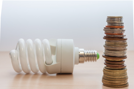 On the table is a light bulb, a stack of coins of different countries, of different dignity, color and size.の写真素材