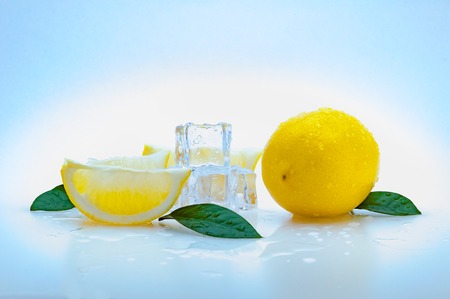 a whole fresh yellow lemon, slices of lemon, green leaves, cubes of cold ice, and on a blue background. isolated.の写真素材