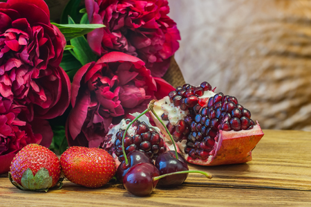 Still life in red tones. Peonies, pomegranate, cherry and strawberry. On a wooden table.の写真素材