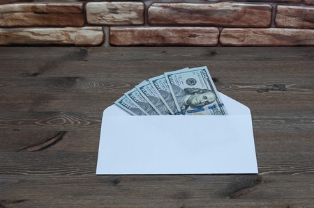 White envelope with five hundred dollars on a wooden table near a brick wall.の写真素材