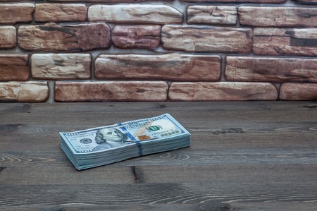 A pack of new American dollars on a table near a red brick wall.