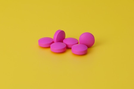 Several large bright pink tablets on a yellow background. In the center of the image.