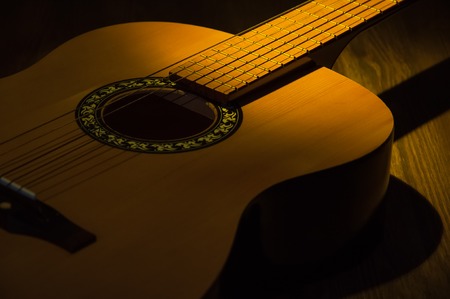 A beam of light illuminates an guitar on a wooden table.の写真素材