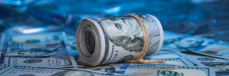 A roll of bills of one hundred dollars tied with a rope on a blue background lies on scattered bills.の写真素材