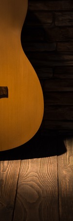 A beam of light illuminates an acoustic guitar standing against a wall on a wooden floor.の写真素材