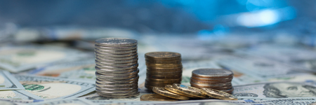Stacks of coins on scattered hundred dollar bills on a blue background